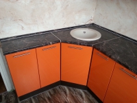 Оранжевая угловая кухня с накладной мойкой белого цвета
